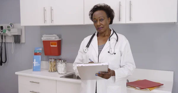 Portrait of senior African-American medical doctor holding clipboard in office