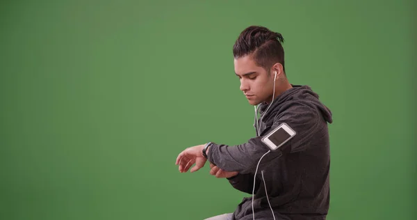 Hispanic Jogger checking fitness tracker while resting on green screen