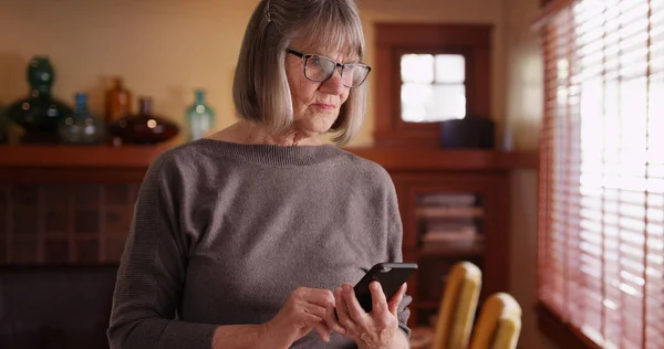 Seriózní Starší Žena Pomocí Telefonu Čtení Tragickou Zprávu Stojící Obývacím — Stock fotografie
