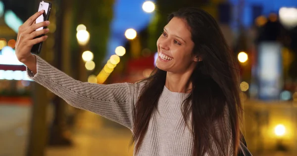 Millennial woman on Champs-Elysees taking selfie with mobile phone at night