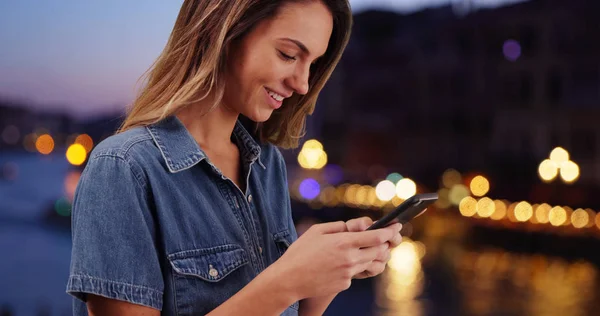 Smiling Caucasian woman using mobile phone outdoors at night