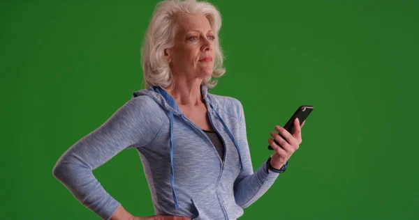 Elderly white female in hoodie using mobile device on green screen