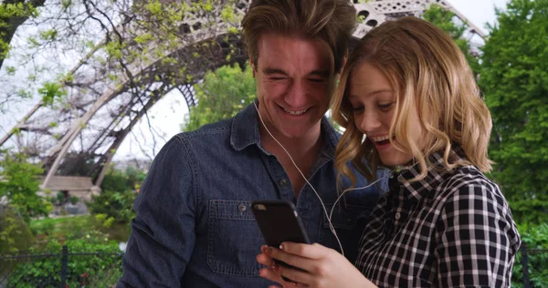 Couple in Paris wear earbuds listening and watching funny video on smartphone