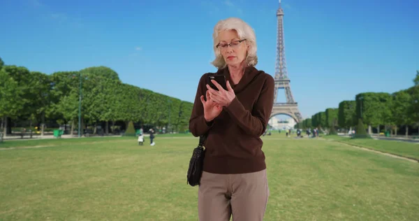 年配の女性観光客がパリでエッフェル塔によって携帯電話で携帯電話の地図アプリをチェック — ストック写真
