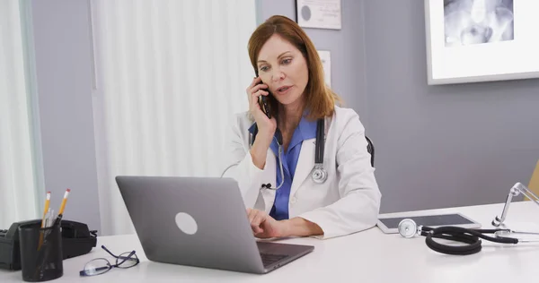 Attractive Mid Aged Doctor Using Latop Computer While Talking Smartphone — Stock Photo, Image