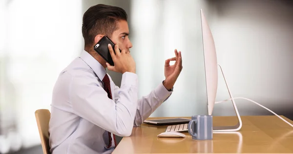 携帯電話で話しながらコンピューターで作業するヒスパニック ビジネス男性 — ストック写真
