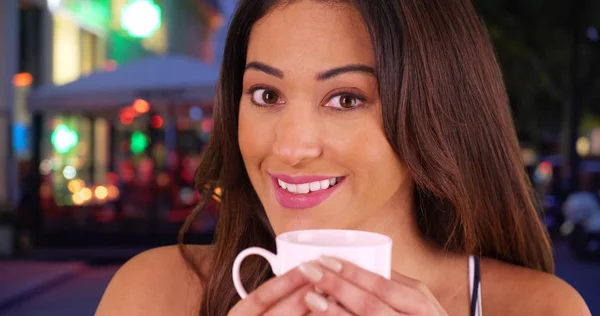 Flirty young Latina woman drinking coffee and looking at camera