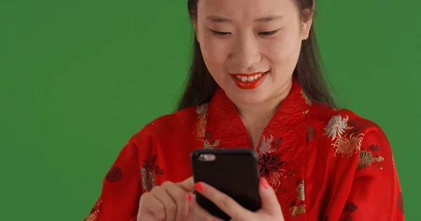 Portrait of happy Chinese woman texting on phone on green screen