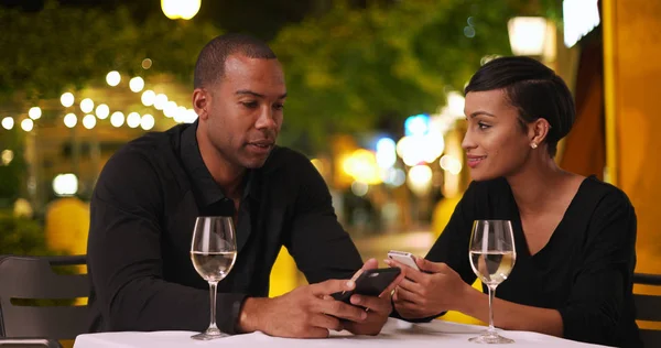 Casual African-American couple talk while using smartphones on date