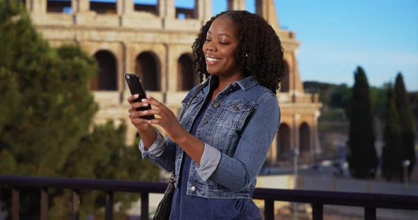 Pretty black female traveling in Rome smiles at cute text from boyfriend