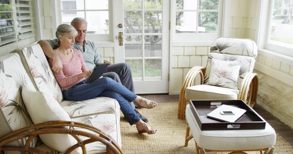 Elderly couple relaxing using tablet on couch at home