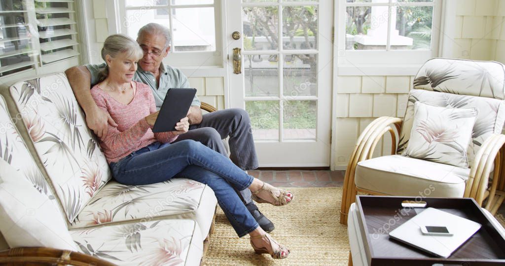 Elderly couple relaxing using tablet on couch at home