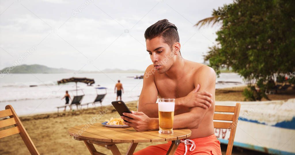 Millennial Hispanic man on tropical vacation drinking beer and eating at beach