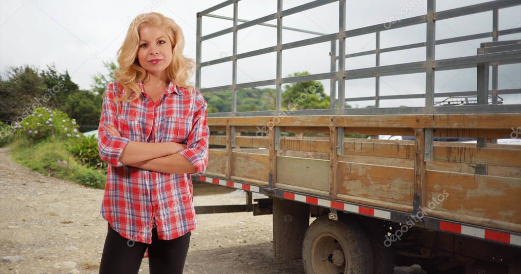 Cheerful Caucasian woman standing by farm truck smiling at camera
