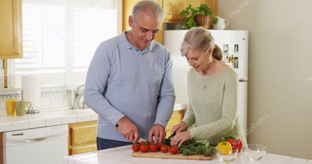 Senior couple cutting vegetables in kitchen