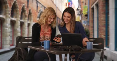 İki sevimli genç yetişkin kadın cep telefonu harita Avrupa street Cafe'de arıyor