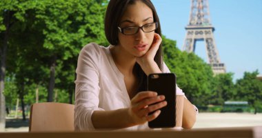 Çekici Latin kadın telefonunu Eiffel Tower yakınındaki iletilerde denetler