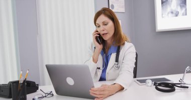 Orta yaşlı Doktor smartphone üzerinde konuşurken latop bilgisayar kullanarak çekici