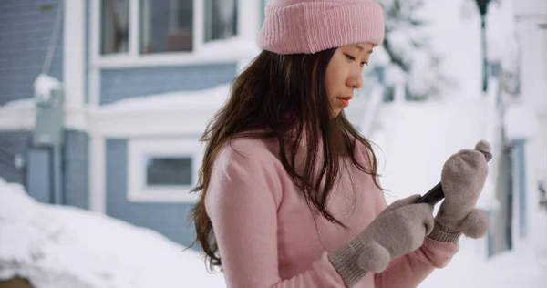 Close up of Asian millennial using smartphone on snow covered street