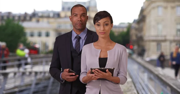 Professional black man and woman holding tech outside on Paris street