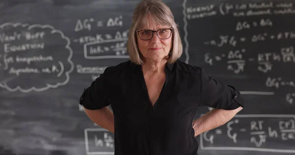 Old senior woman teacher with serious attitude posing in front of chalkboard