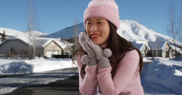 Cute woman sitting in pose with mittens and beanie on snow covered street