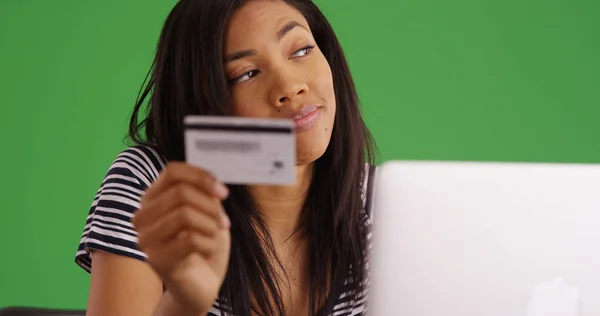 Young black woman with credit card shopping online on laptop on green screen