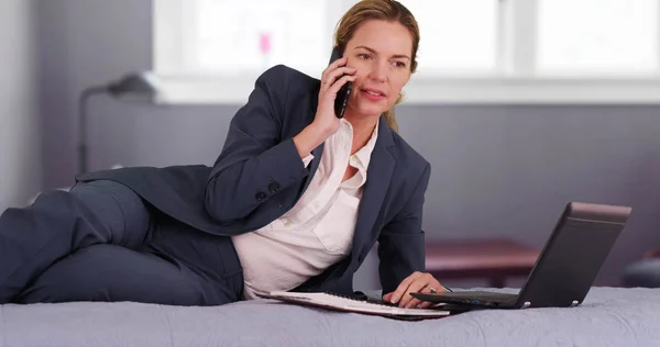 Successful woman in business suit making phone call from bedroom