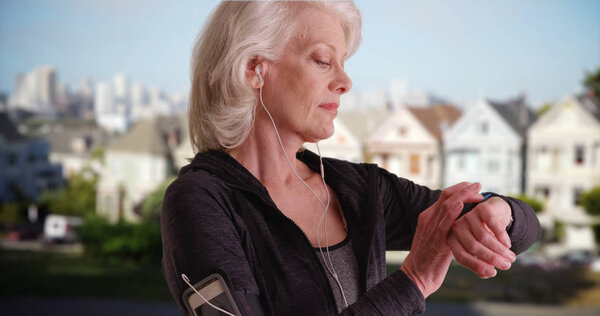 Athletic senior woman out jogging in San Francisco looking at watch outside