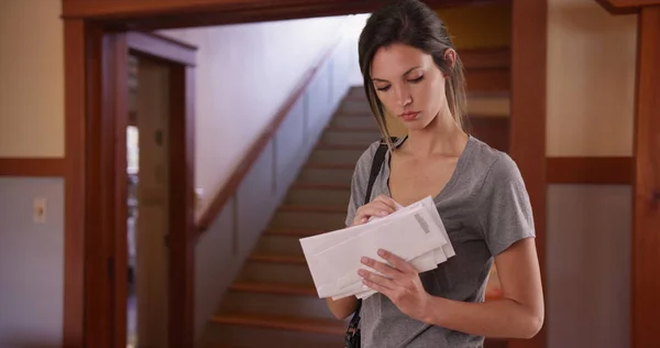 White millennial female checking stack of letters standing inside her house