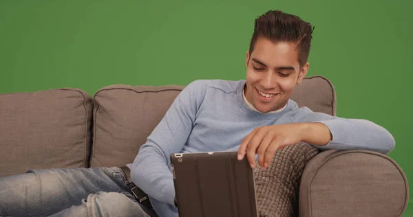 年轻的西班牙男子坐在沙发上使用平板电脑在绿色屏幕上 — 图库照片