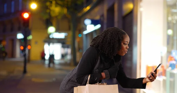 Black woman stops to take picture of something cute in window display at night