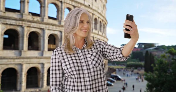 Middle-aged caucasian female takes selfie on phone at Colosseum in Rome