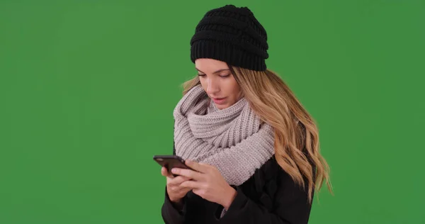 Millennial woman in winter clothes texting on smartphone on green screen