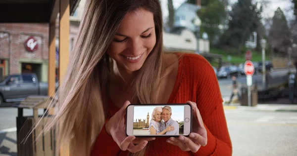 Happy white female with phone showing video of parents vacationing in England