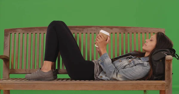 緑色の画面の上にコーヒー カップを保持しているベンチに横になって若い女性 — ストック写真