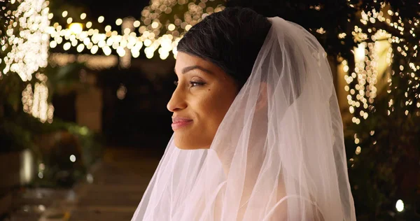 Profile of lovely bride in wedding veil standing outside romantic venue at night