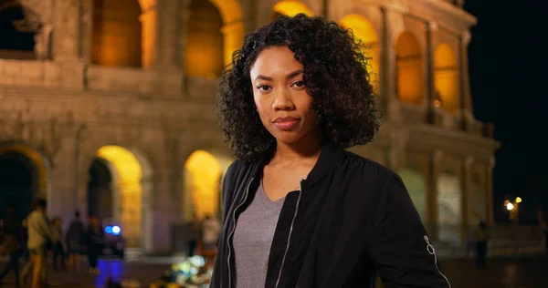 African American woman on vacation standing outside Colosseum in Rome at night