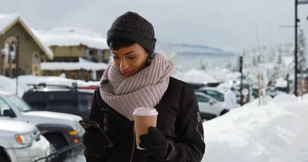 Beautiful young woman in the snow with coffee using smartphone