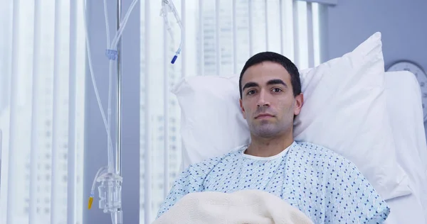 Adult male latino patient lying on hospital bed and looking at camera