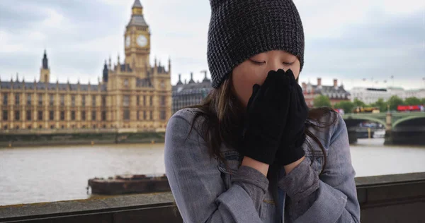 Close up of Asian millennial wearing beanie and mittens near Big Ben in London