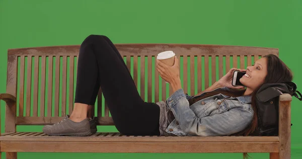 Pretty girl lying down on bench talking on cellphone on green screen