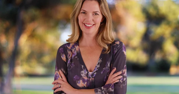 Caucasian woman in blouse standing in park in autumn smiling at camera