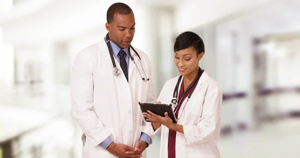 两位专业的非裔美国医生在使用平板电脑时交谈 — 图库照片