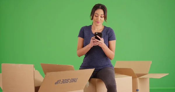 緑色の画面で携帯電話を使用してボックスを開梱しながら休憩を取って ラティーナの女性 — ストック写真