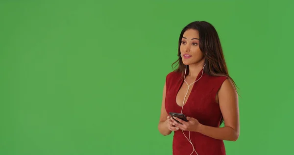 Attractive Latina female listening to music on smartphone on green screen