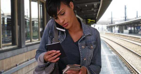 Traveling black female waiting at metro station with passport chats on smartphone