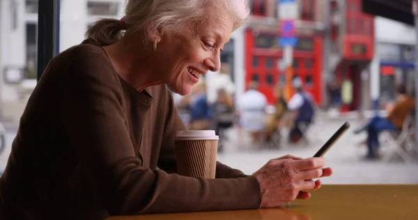 Happy senior woman receives good news via text while waiting in coffee shop