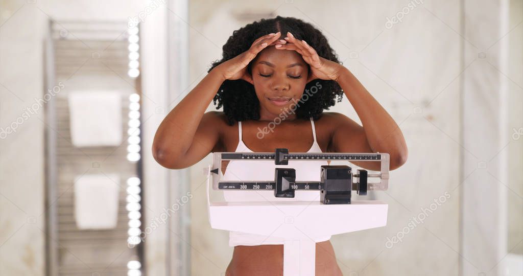 Young black woman weighs herself on scale frowning and shaking her head