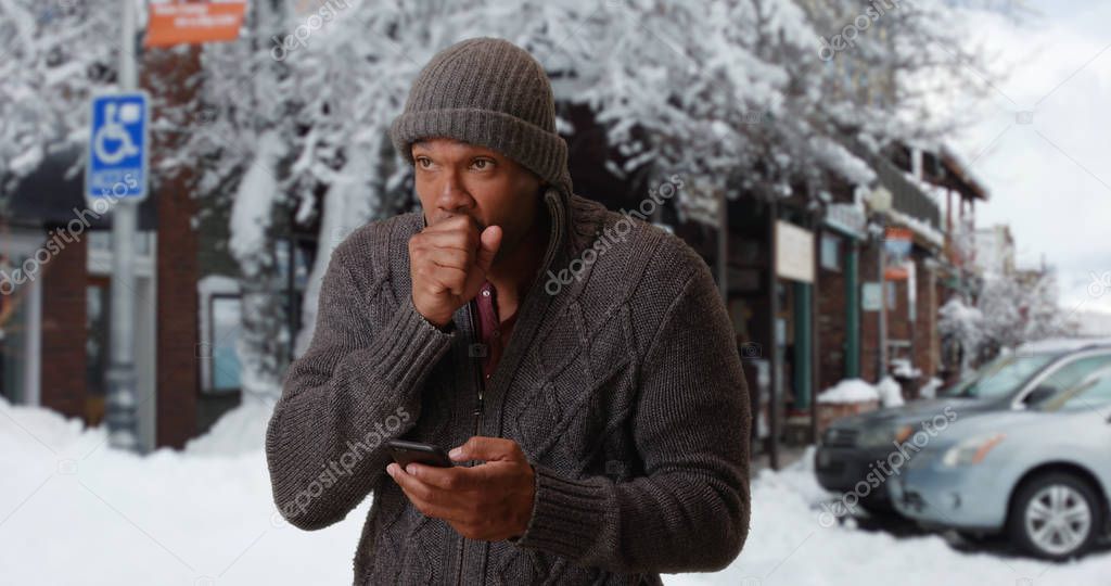 Portrait of black man sending text message on cellphone in snowy setting